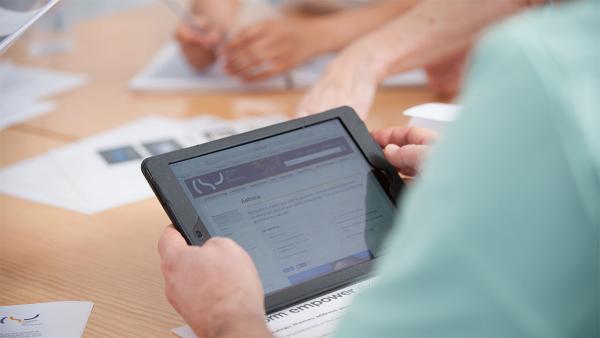 Close-up of hands round a table looking at a tablet and paperwork