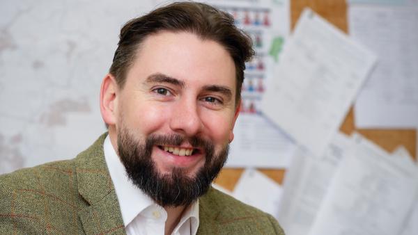 Photo of David Williams in front of an office notice board