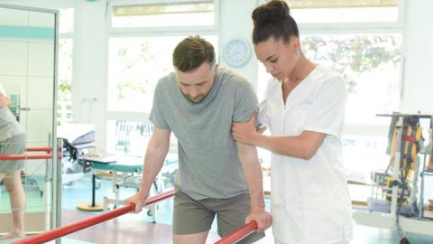 Practitioner helping a patient to support themselves on bars